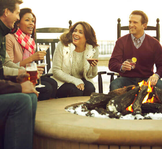 Group of adults sitting around a firepit drinking cocktails